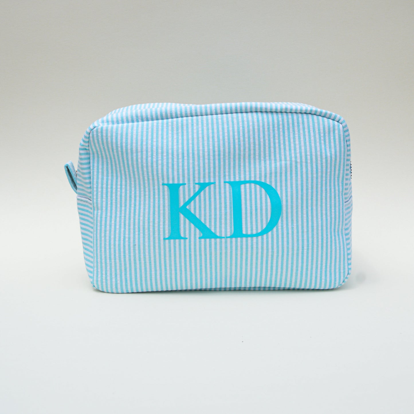 Light blue striped pouch with 'KD' monogram on a white surface with a blue sky background