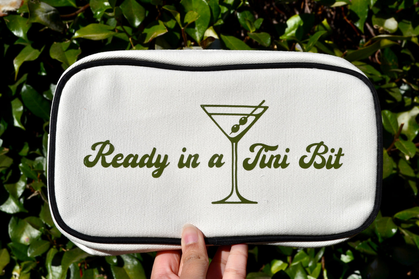 White pouch with 'Ready in a Tini Bit' text and martini glass design held against a green leafy background
