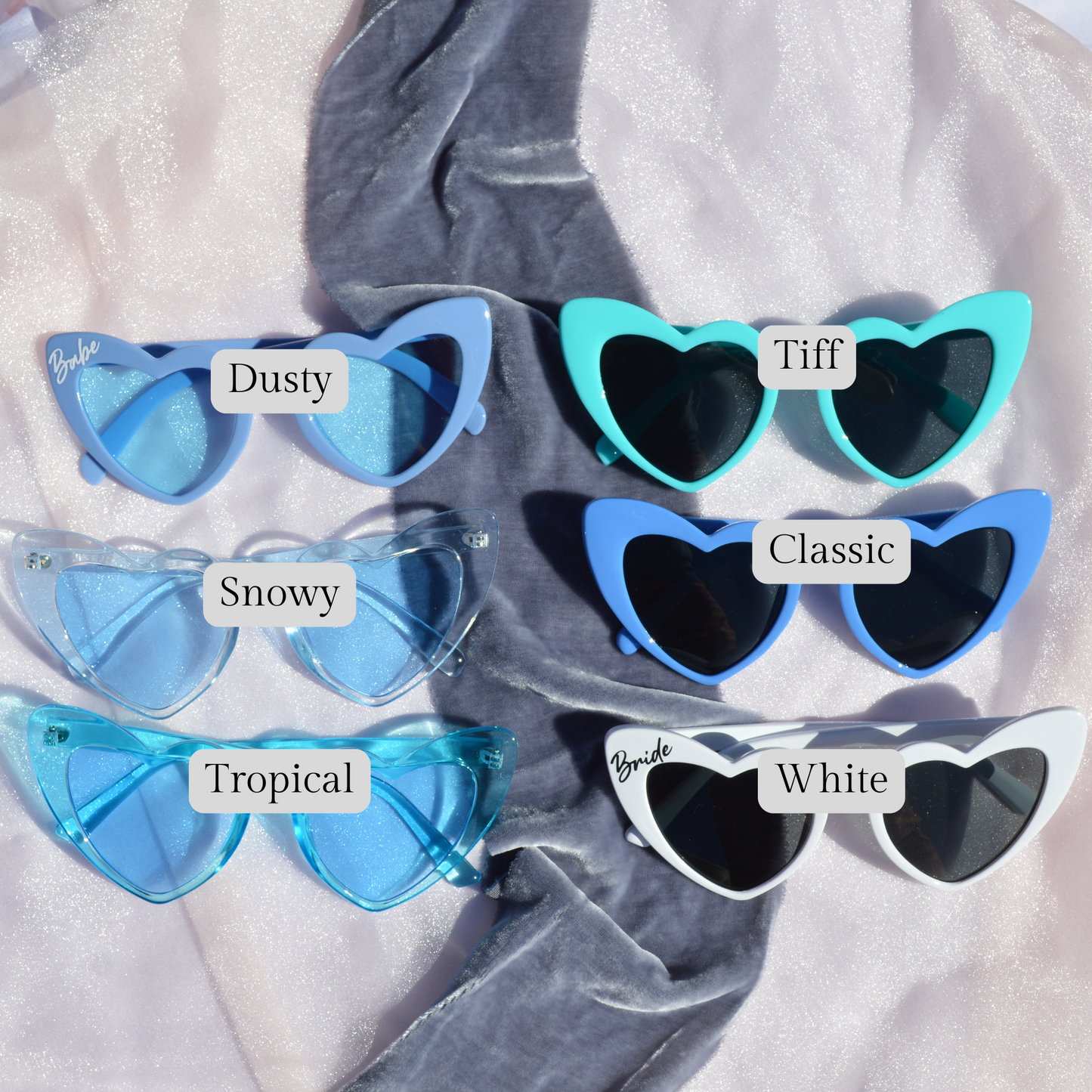 Heart-shaped sunglasses with labeled color options on a textured fabric background