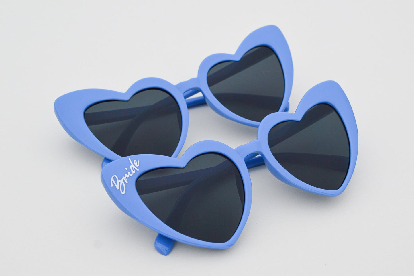 Blue heart-shaped sunglasses with dark lenses on a light gray background