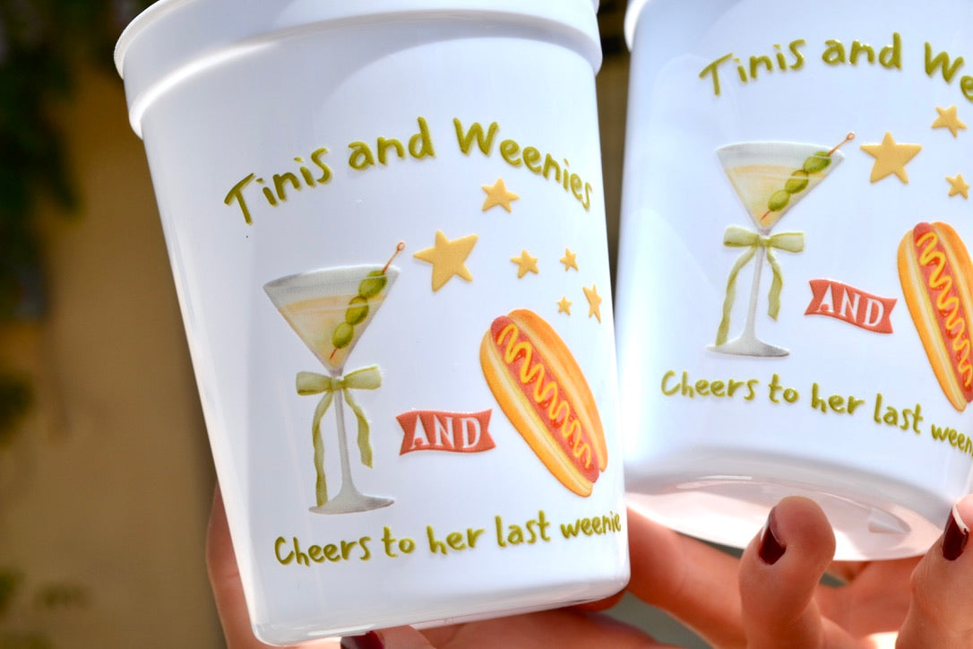 Two white cups with decorative designs and text, held by a person.