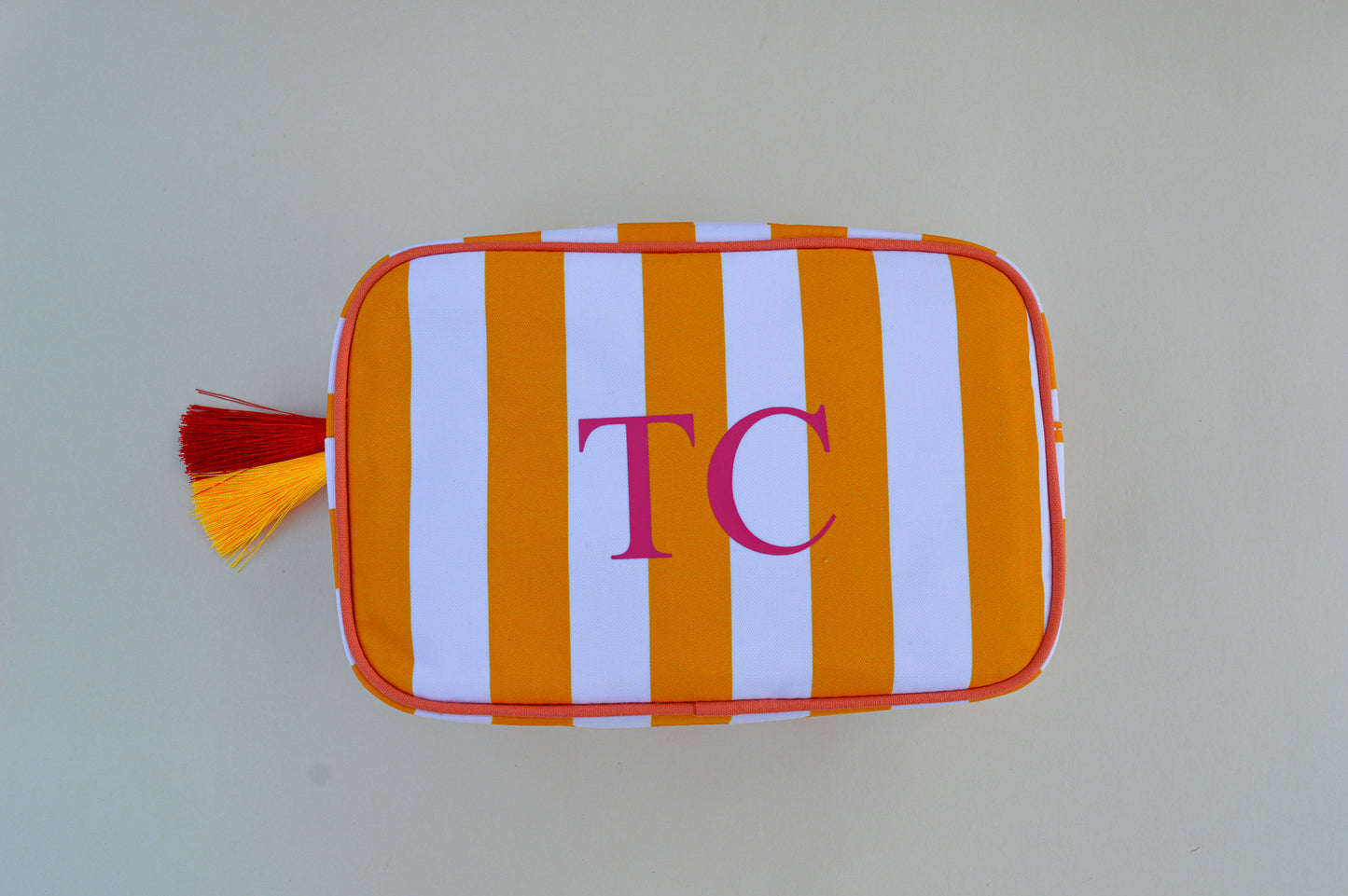 Striped pouch with orange and white stripes and red tassel on a light gray background