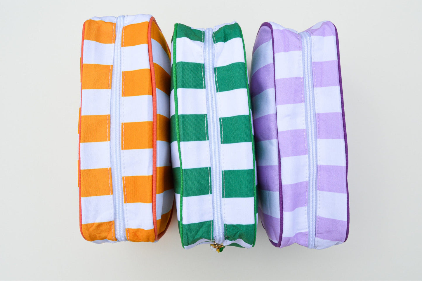 Three striped pencil cases in orange, green, and purple on a white background