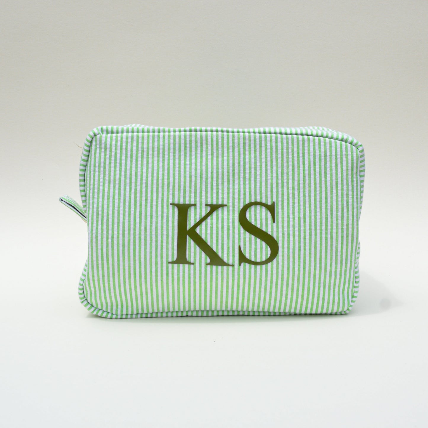 Green striped pouch with 'KS' initials on a white surface with blue sky background