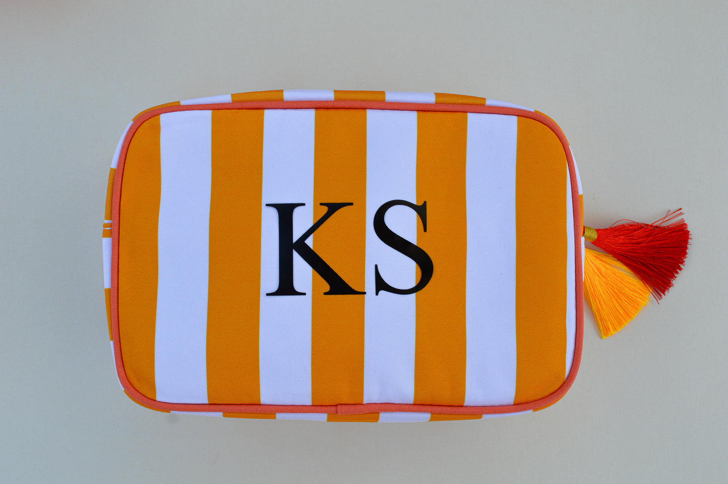 Striped pouch with 'KS' monogram and tassels on a plain background