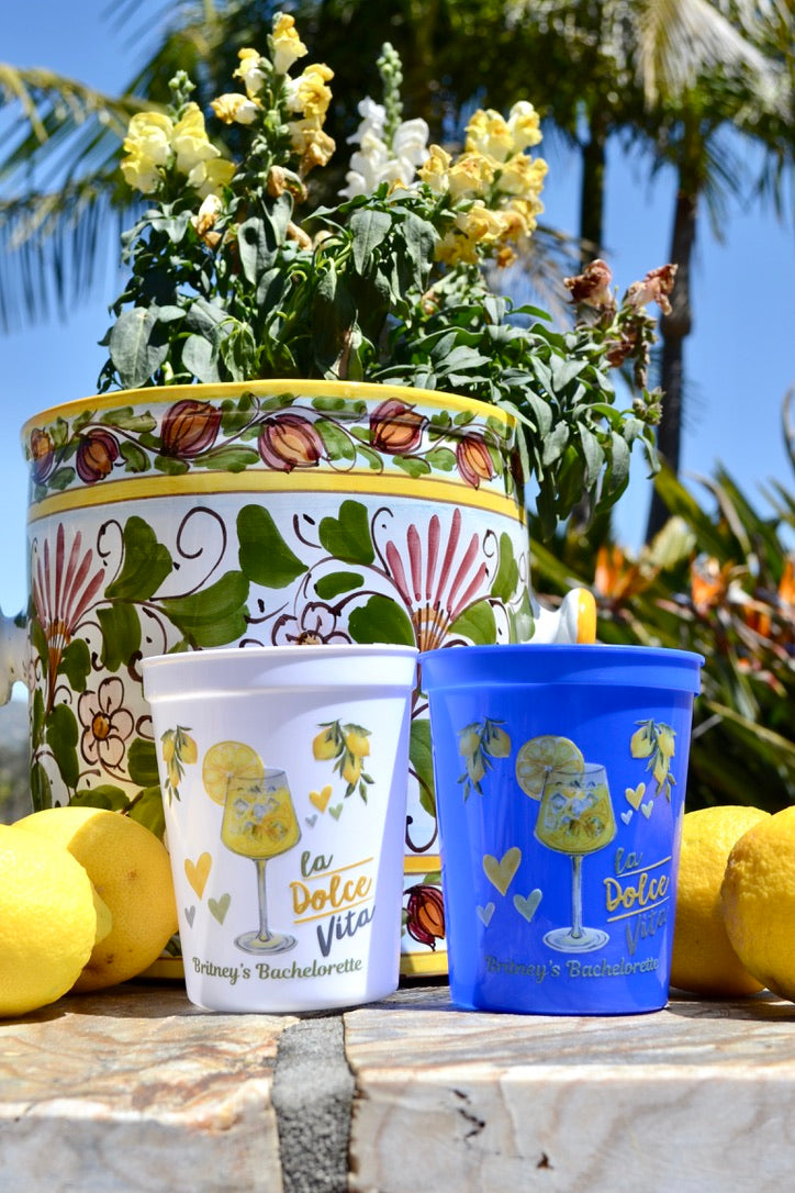 Two Italian Summer cups with a decorative pot and lemons on a wooden surface.