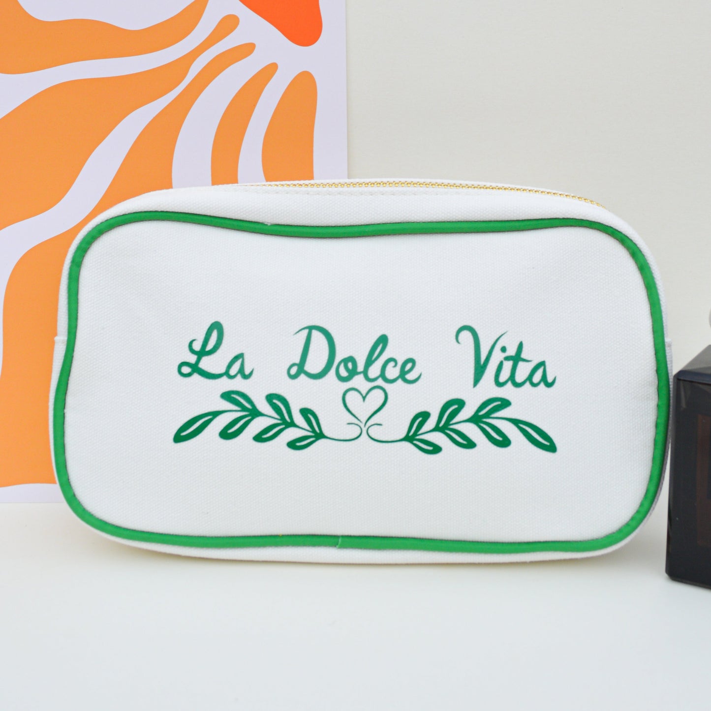 Product display with 'La Dolce Vita' sign, orange abstract design, and small bottle on a light background