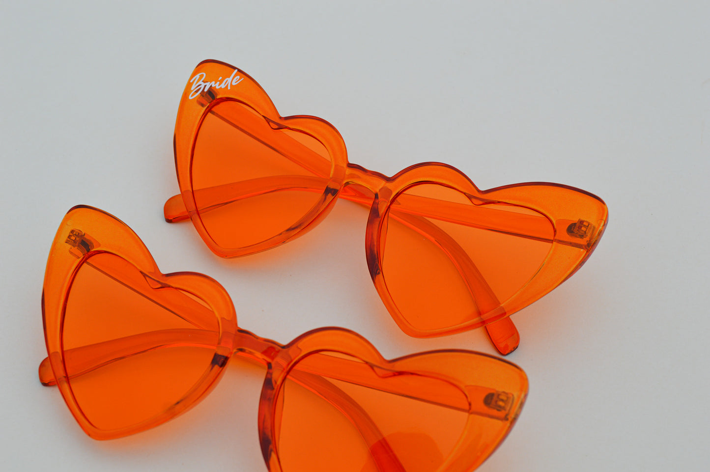Orange heart-shaped sunglasses with 'Bride' text on a light gray background