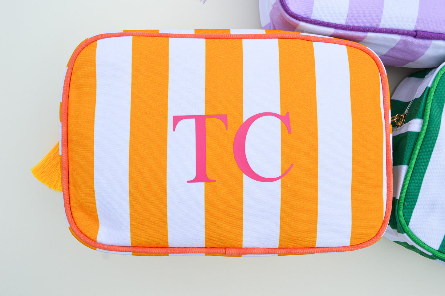 Orange and white striped pouch with pink initials 'TC' on a light gray background