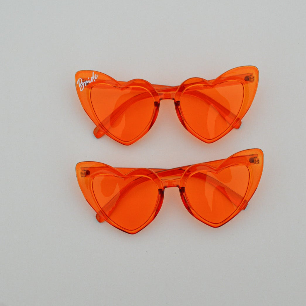 Pair of orange heart shaped sunglasses on a light gray background