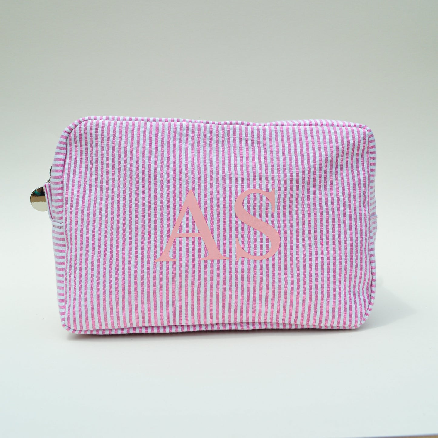 Pink striped pouch with initials 'AS' on a light gray surface with white background