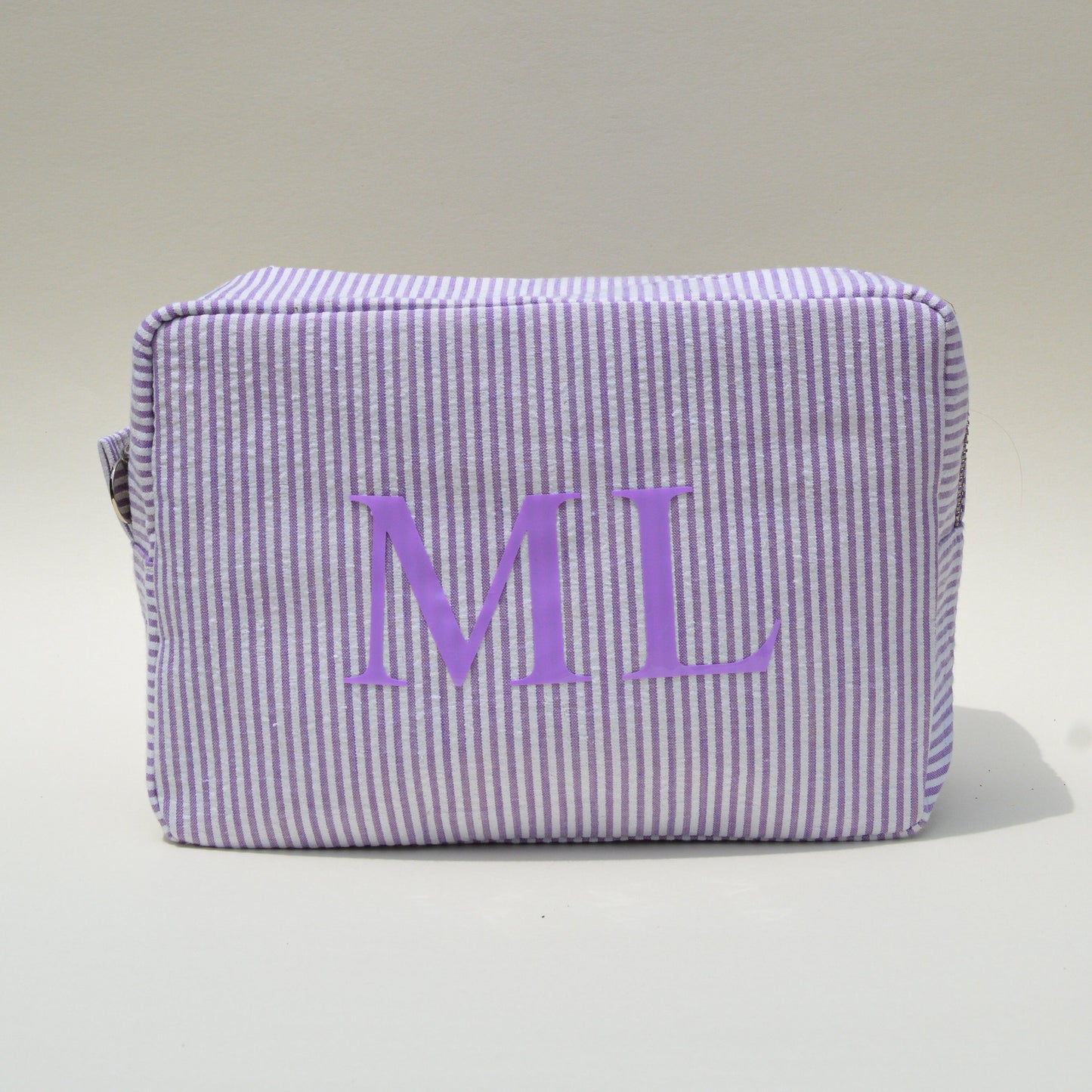 Purple striped pouch with 'ML' initials on a white surface with blue sky background