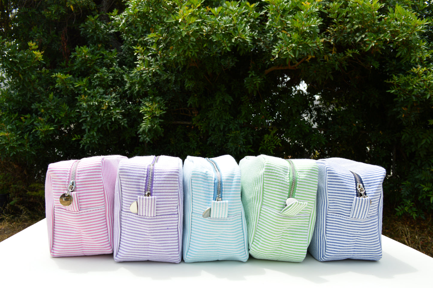 Set of pastel-colored bags with striped patterns on a white surface outdoors.