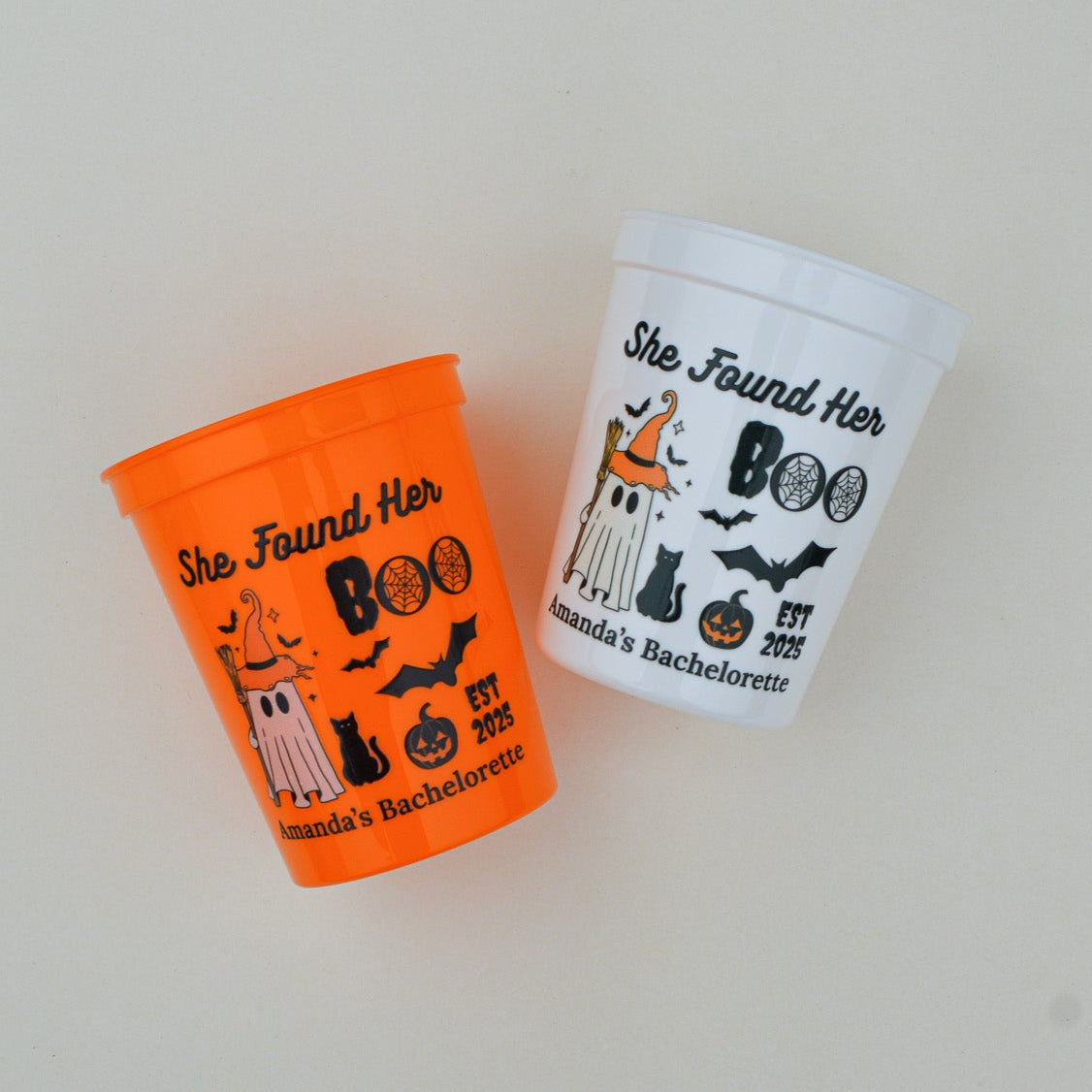 Two Halloween-themed cups, one orange and one white, on a light gray background.