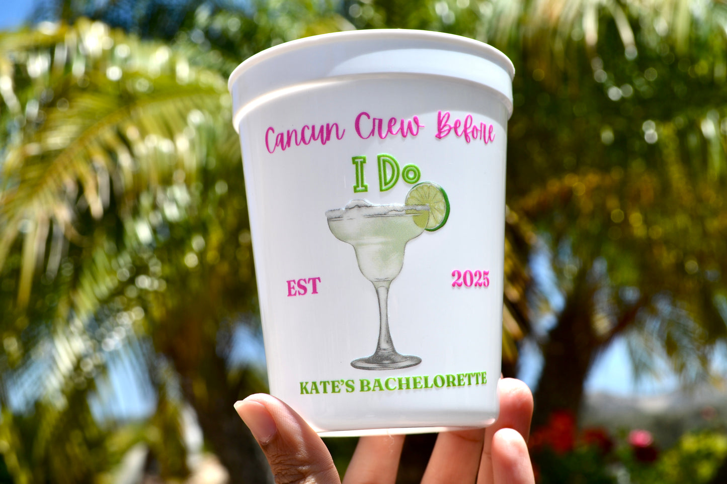 Personalized bachelorette party cup with margarita design and text, held in front of palm trees.