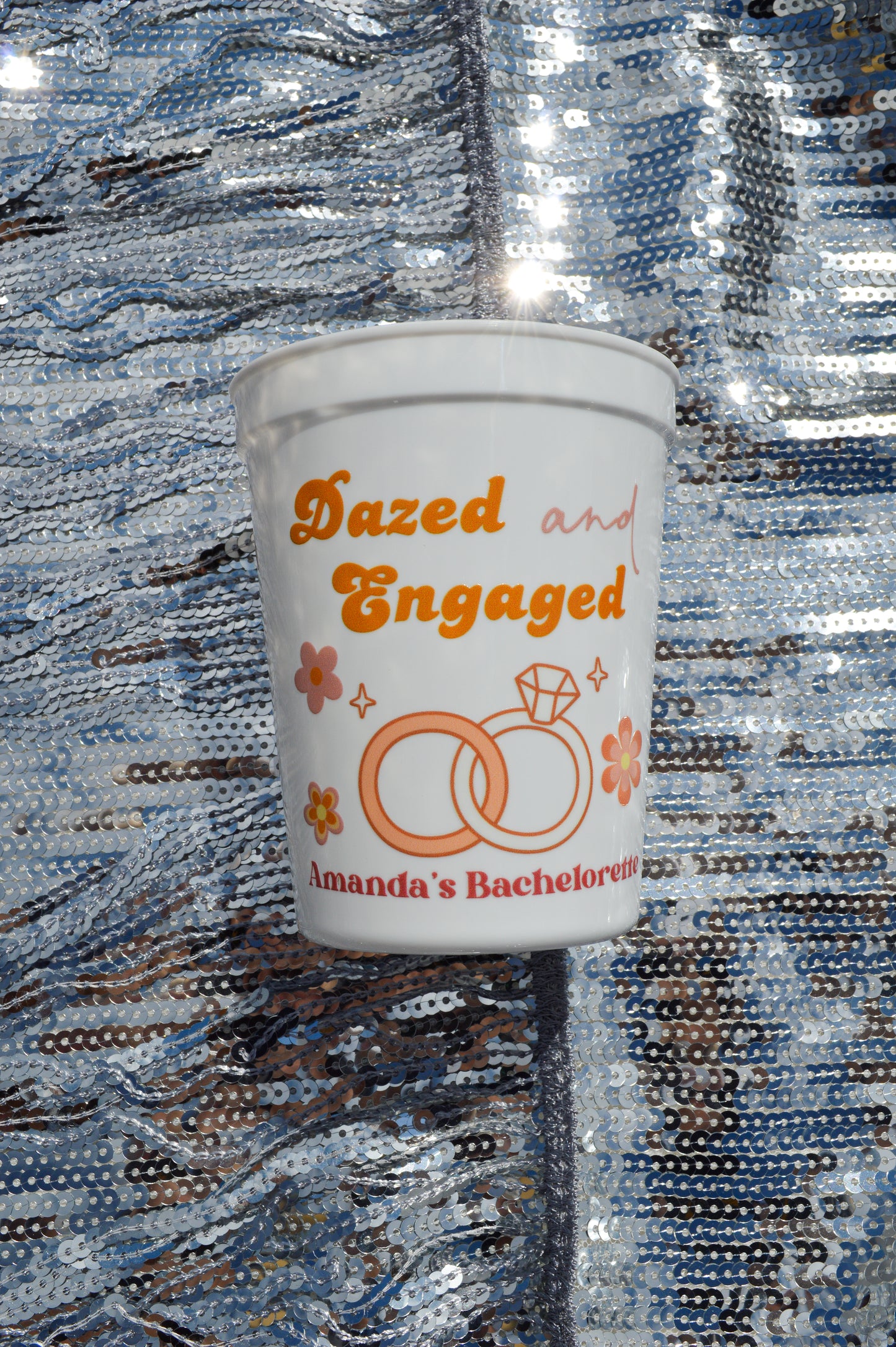 White cup with 'Dazed and Engaged' text and ring design on a reflective surface