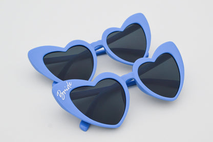 Blue heart-shaped sunglasses with dark lenses on a light gray background