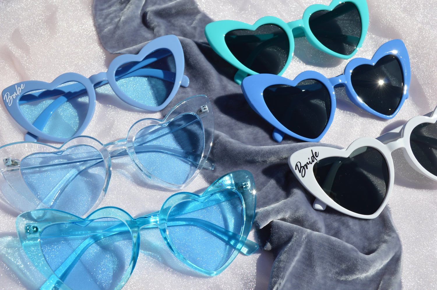 Heart-shaped sunglasses in various colors on a gray fabric background