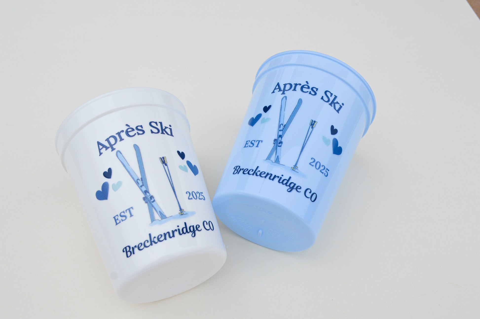 Two blue and white cups with skiing design and text on a light gray background