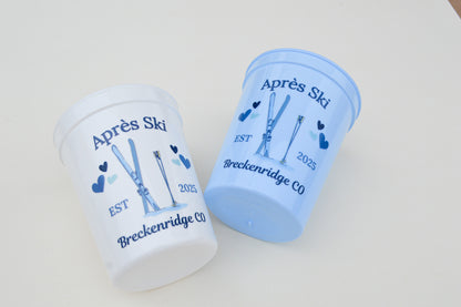 Two blue and white cups with skiing design and text on a light gray background