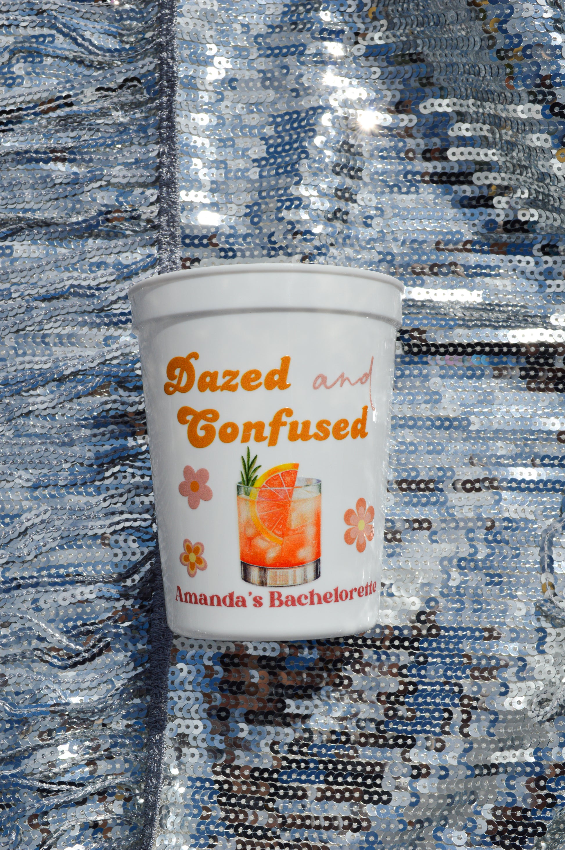 White cup with 'Dazed and Confused' text and cocktail graphic on a sequined background