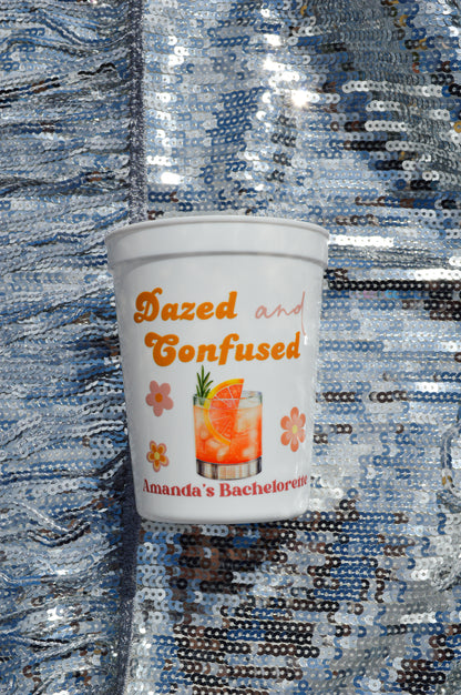 White cup with 'Dazed and Confused' text and cocktail graphic on a sequined background