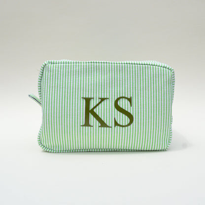 Green striped pouch with 'KS' initials on a white surface with blue sky background