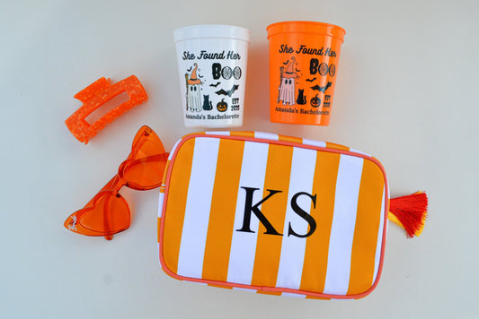Orange and white striped pouch with 'KS' initials, orange cup, and sunglasses on a light gray background
