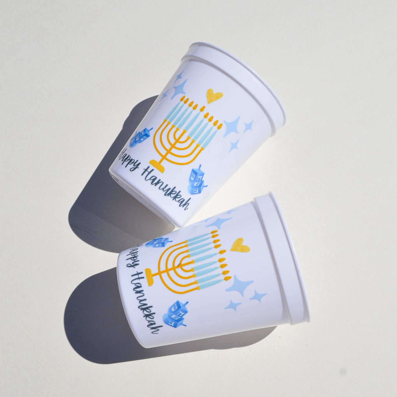 Two white plastic cups with Hanukkah-themed designs on a light surface
