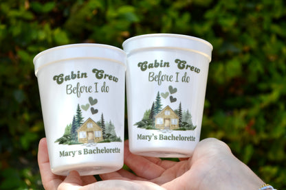 Two personalized cups with 'Cabin Crew Before I Do' text and nature-themed design held against a blurred green background.