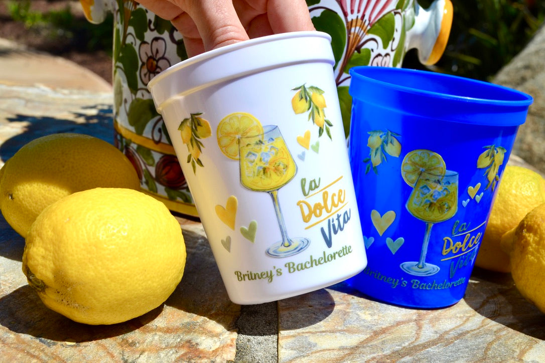 Two cups with lemon-themed designs on a stone surface with lemons around.
