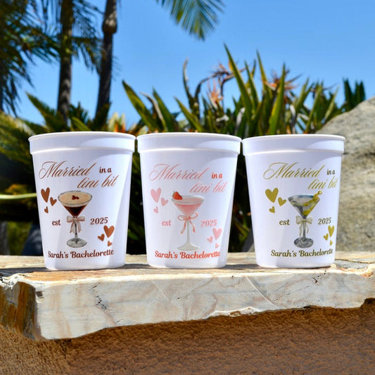 Three personalized cups with bachelorette party designs on a wooden surface with a tropical background.