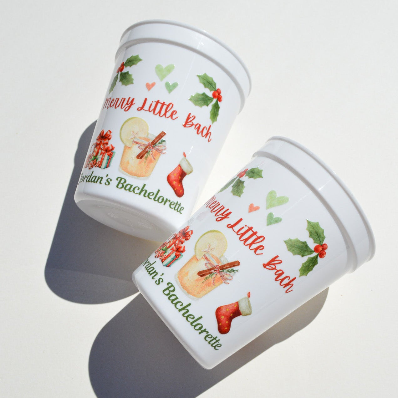 Two white cups with festive designs and text on a light surface.