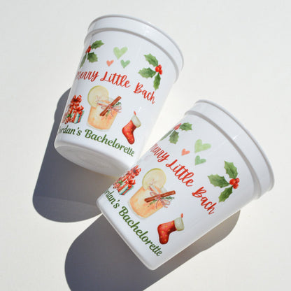 Two white cups with festive designs and text on a light surface.