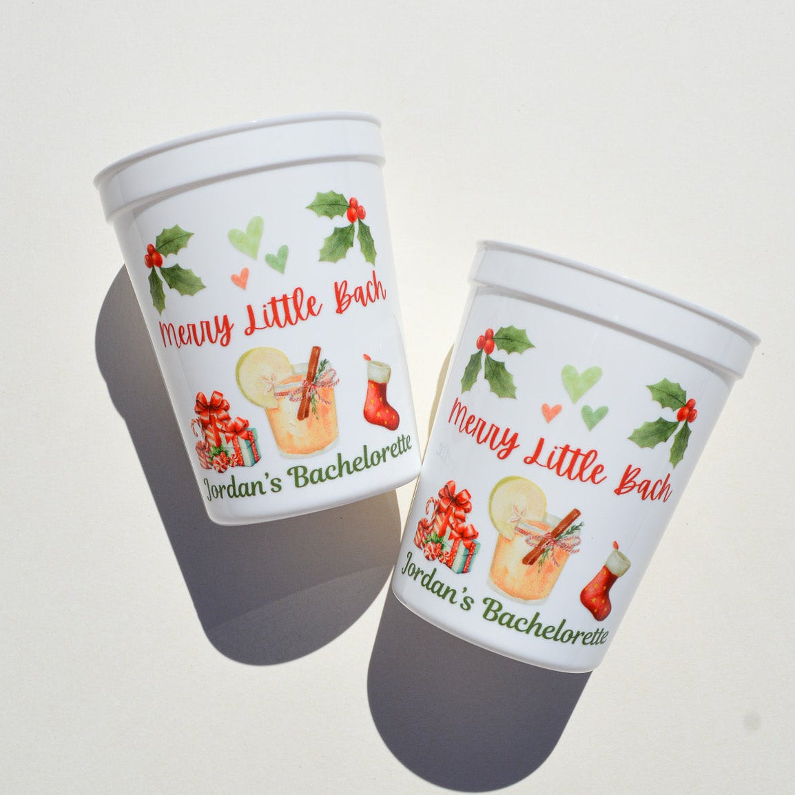 Two white plastic cups with festive designs and text on a light gray background