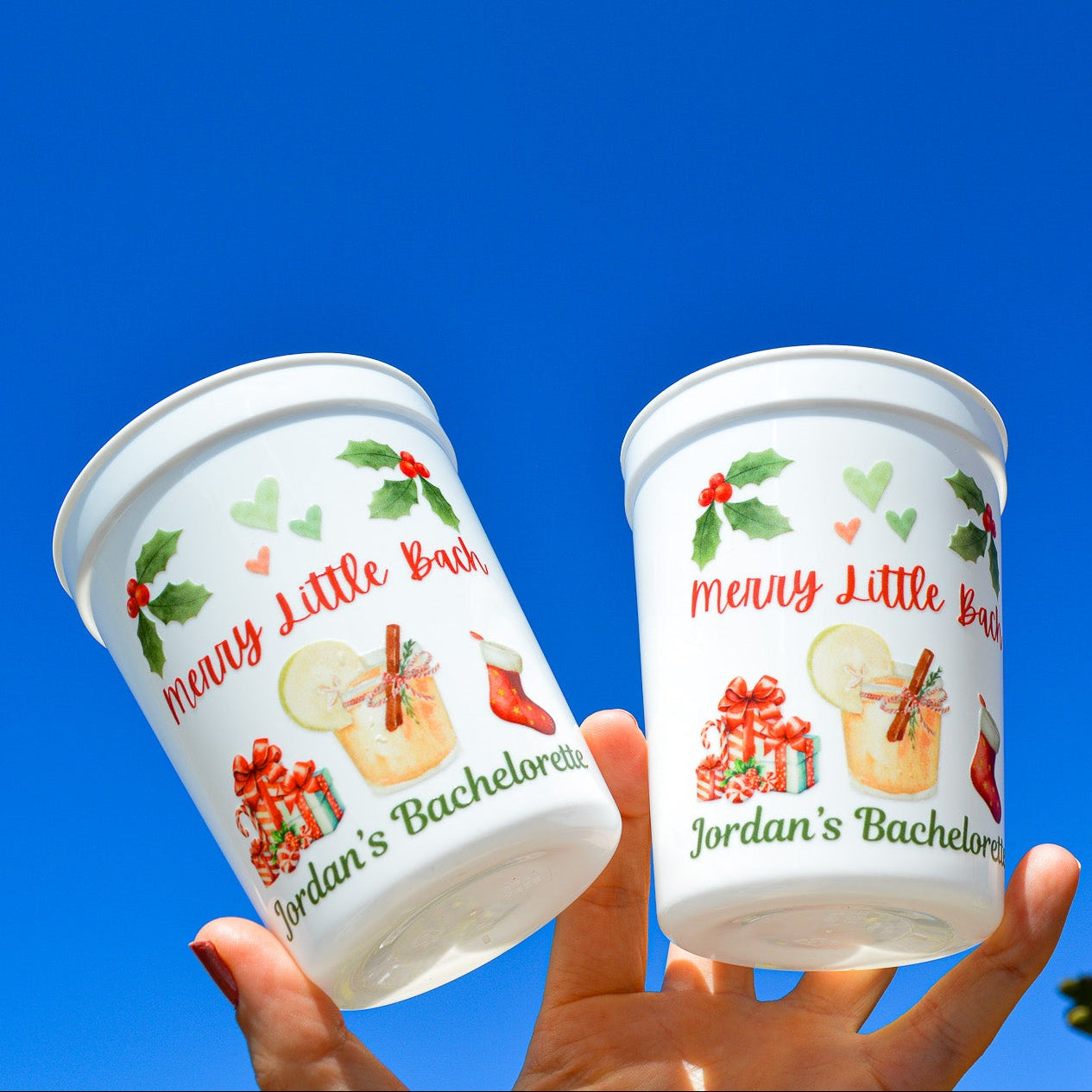 Two white cups with 'Merry Little Bachelorette' design against a blue sky.
