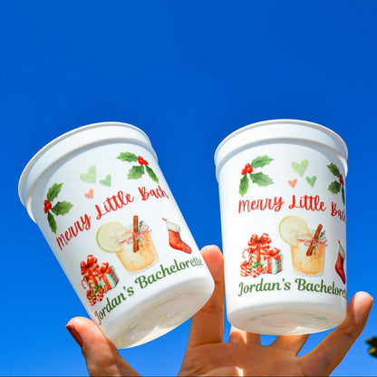 Two white cups with 'Merry Little Bachelorette' design against a blue sky.