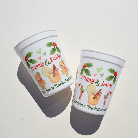 Two festive plastic cups with 'Merry & Bride' text and holiday-themed graphics on a light gray background.