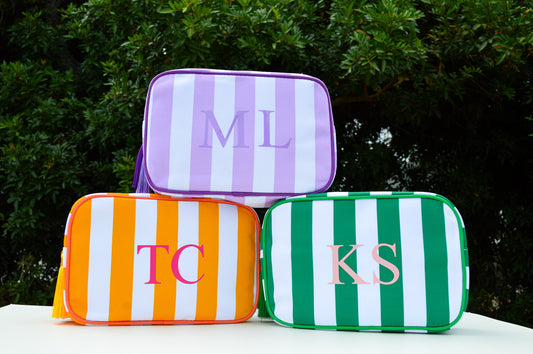 Three striped pouches with initials on a white surface with a green leafy background
