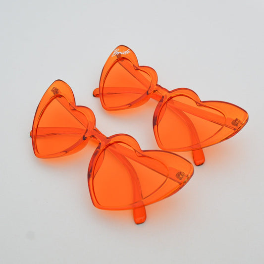 Orange heart-shaped sunglasses on a white surface