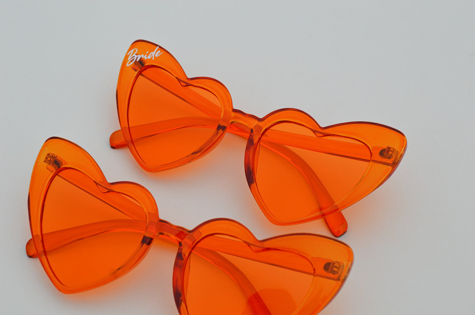 Orange heart-shaped sunglasses with 'Bride' text on a light gray background