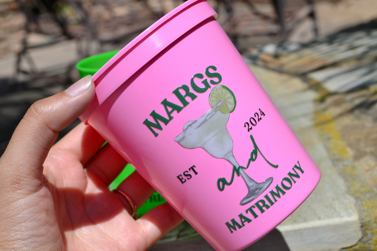 Pink cup with 'Margs and Matrimony' held by a hand against a stone background