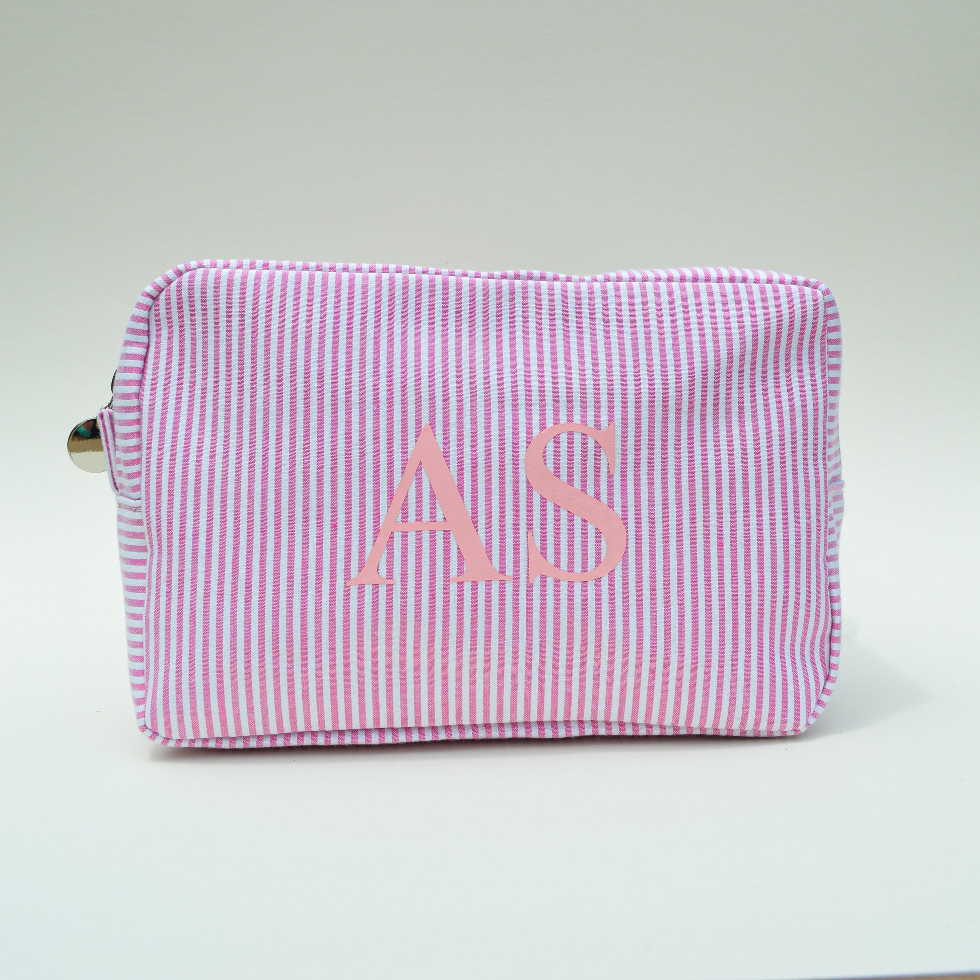 Pink striped pouch with initials 'AS' on a light gray surface with white background