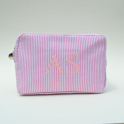 Pink striped pouch with initials 'AS' on a light gray surface with white background
