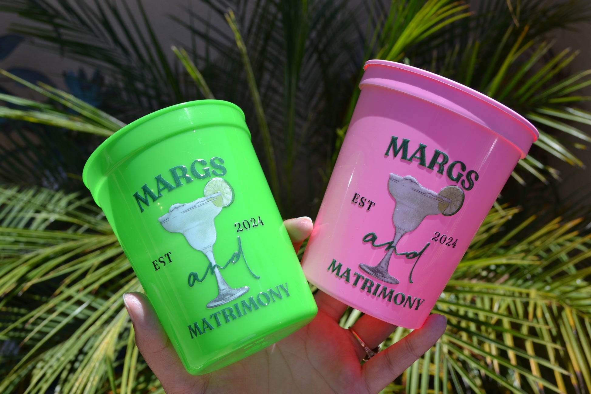 Two colorful cups with 'Margs and Matrimony' branding against a green leafy background