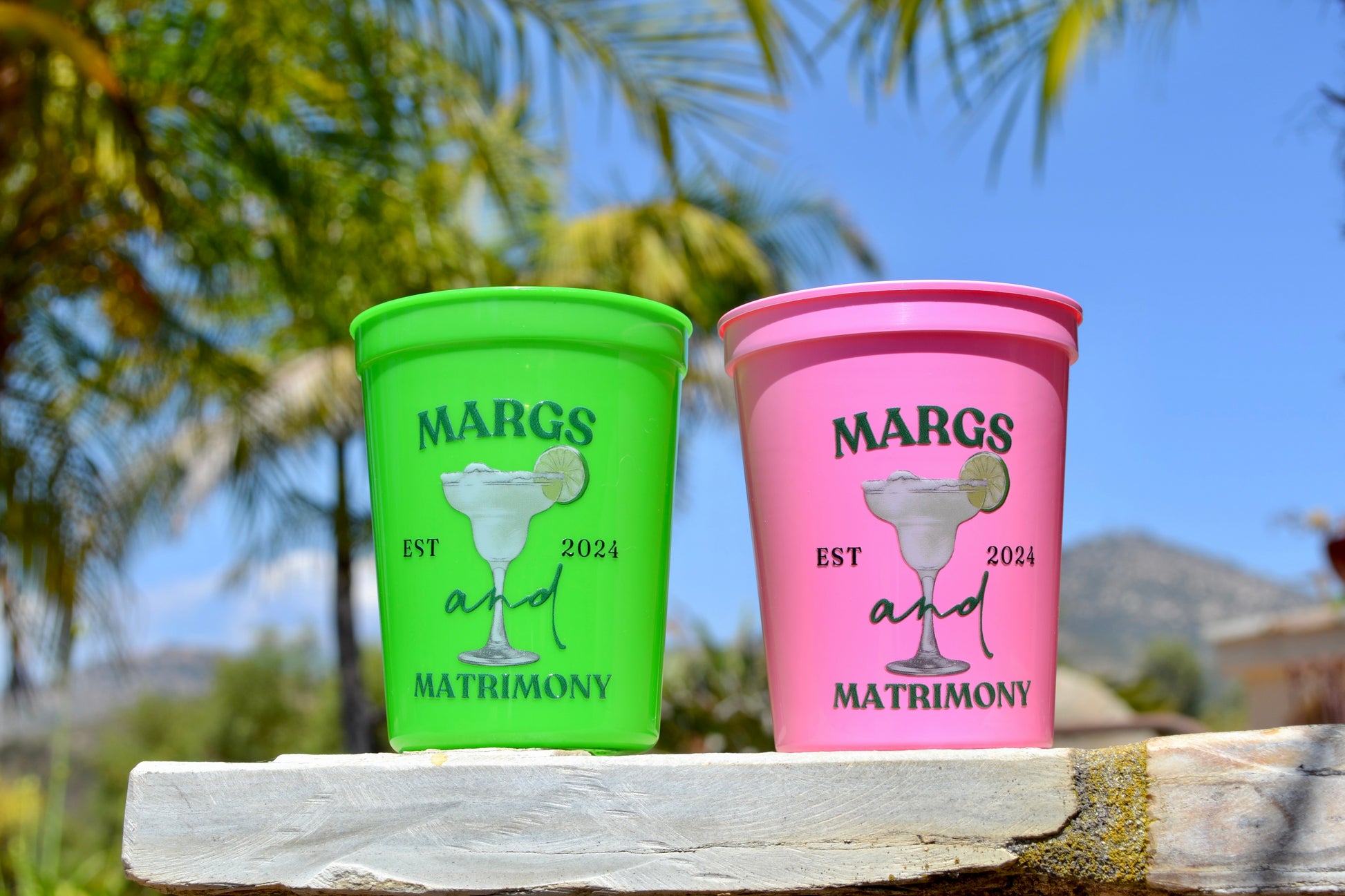 Two colorful cups with 'Margs and Matrimony' text on a natural background.