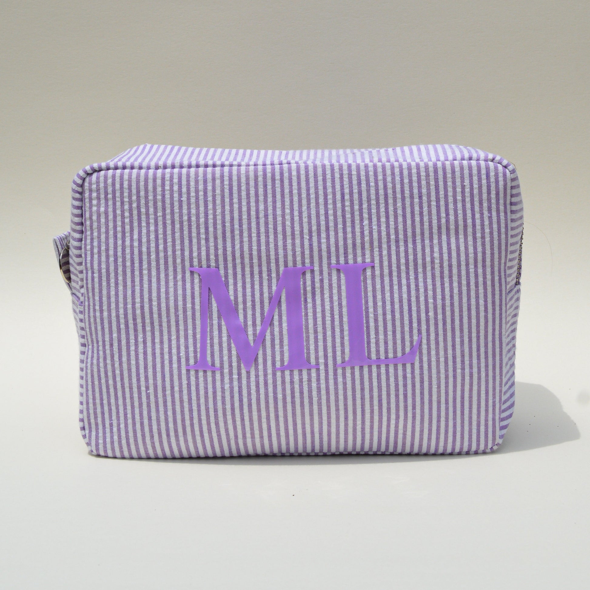 Purple striped pouch with 'ML' initials on a white surface with blue sky background