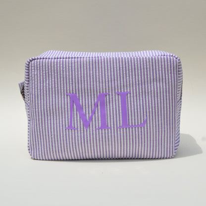 Purple striped pouch with 'ML' initials on a white surface with blue sky background