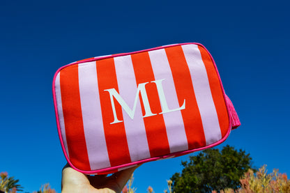 Red and white striped pouch with 'ML' initials held against a blue sky.