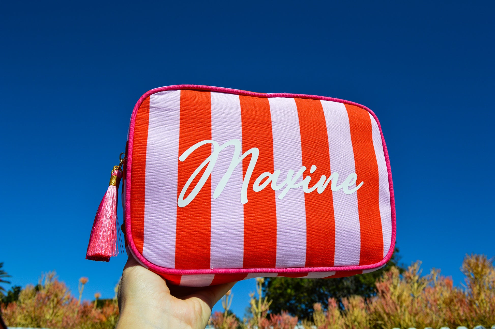 Red and white striped pouch with 'Maxine' branding held against a blue sky.